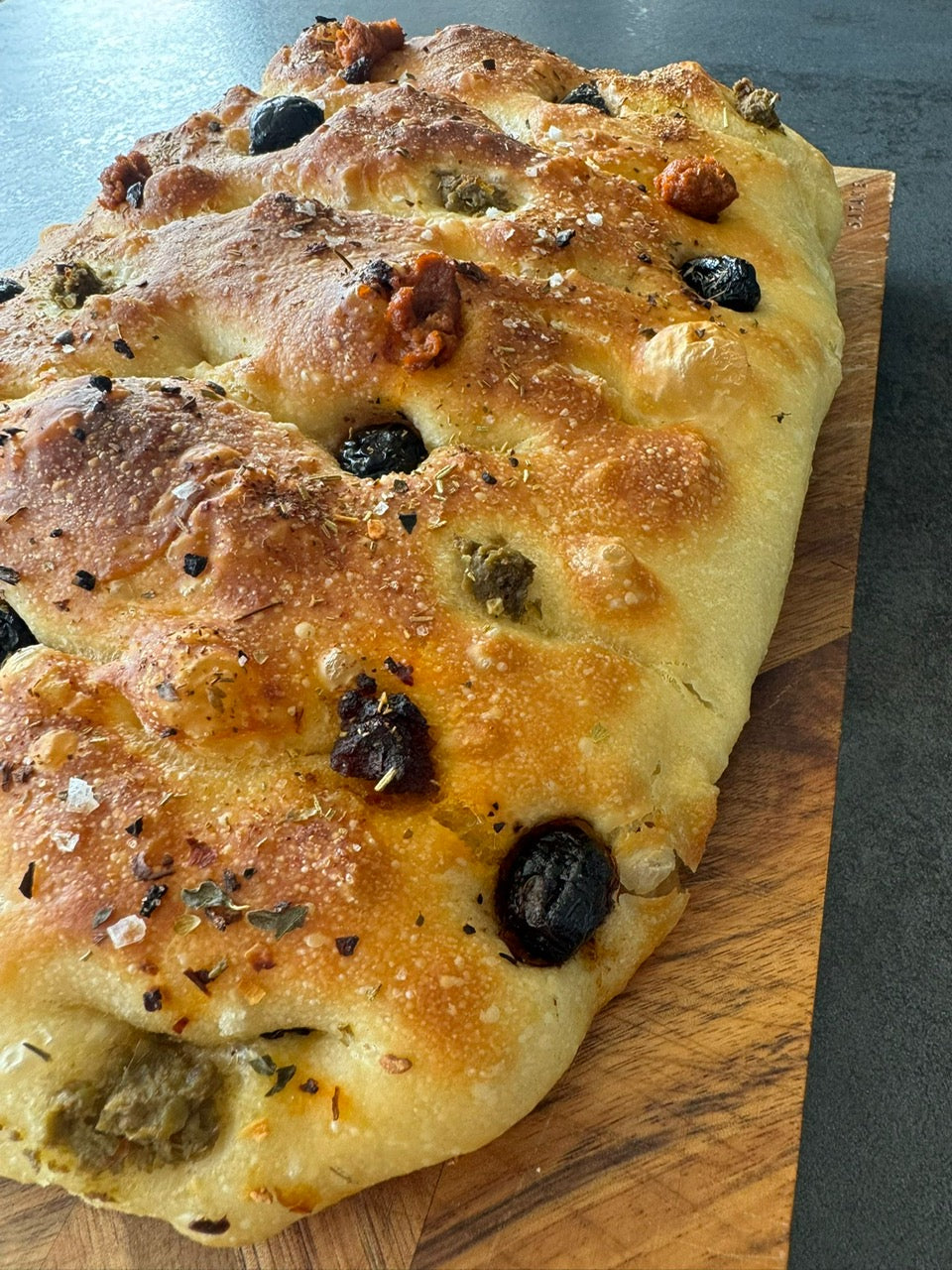 Frisch gebackenes Focaccia mit Oliven und Tomaten auf Holzbrett